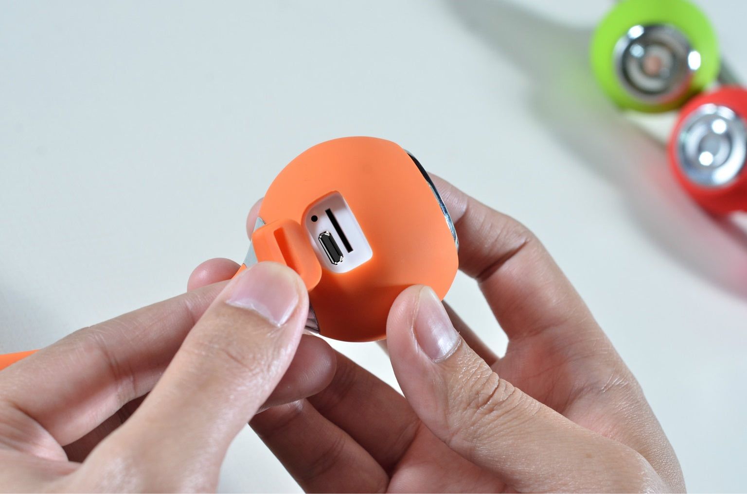 Person holding an orange waterproof Bluetooth speaker showcasing its charging port for outdoor use