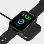 Black smart watch with encoder displaying charging status and digital time on a charging dock