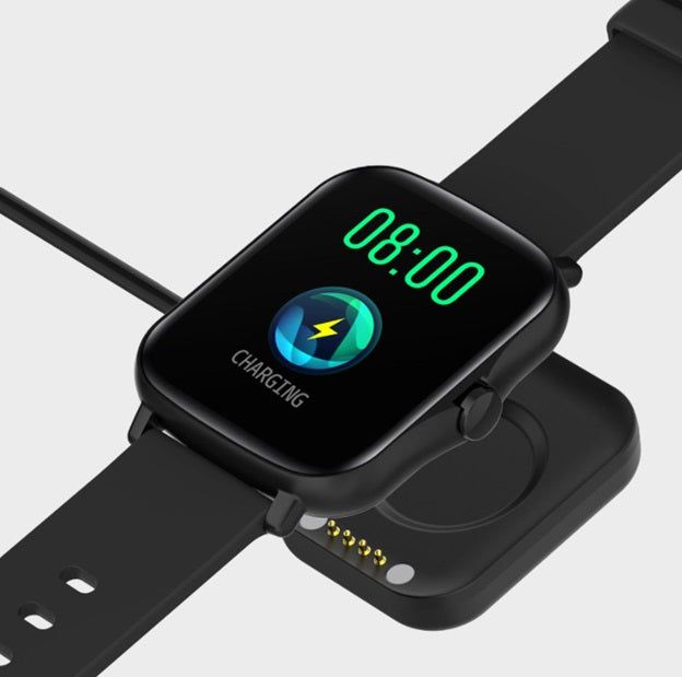 Black smart watch with encoder displaying charging status and digital time on a charging dock